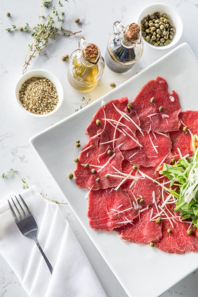 Delicious beef carpaccio with capers, olive oil, and fresh toppings on a white plate.